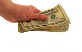 A hand holding a stack of U.S. dollar bills against a white background. A hand holding a stack of U.S. dollar bills against a white background.